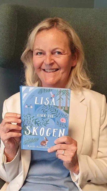Biblioteksansatt sitter i en stol, smiler og viser frem boka "Lisa gikk til skogen"