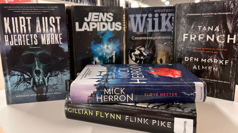På et bord står bøker av Jens Lapidus, Øistein Wiik, Kurt Aust., Mick Herron og Tana French utstilt. Foto.