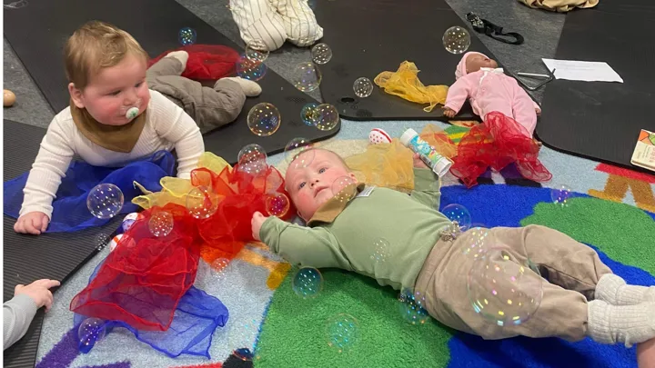 To små babyer ligger på gulvet, såpebobler i lufta over dem. Foto