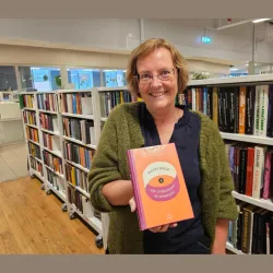 Biblioteksansatt står foran en bokhylle med bøker og viser frem boka Om utregning av romfang. Foto.