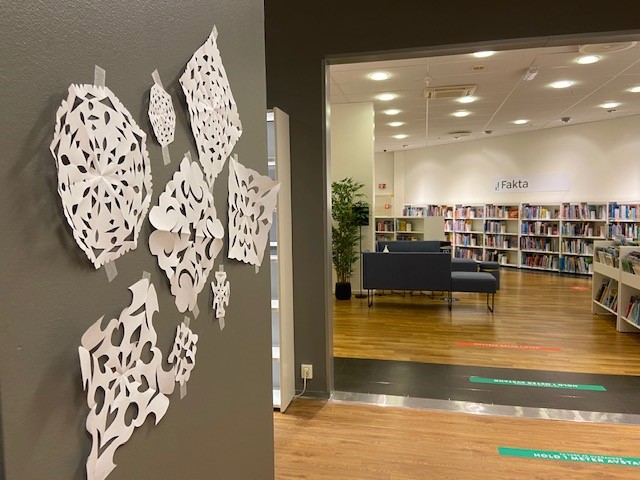 Snøkrystaller i papir henger på en vegg i biblioteket. Hyller i bakgrunnen. Foto