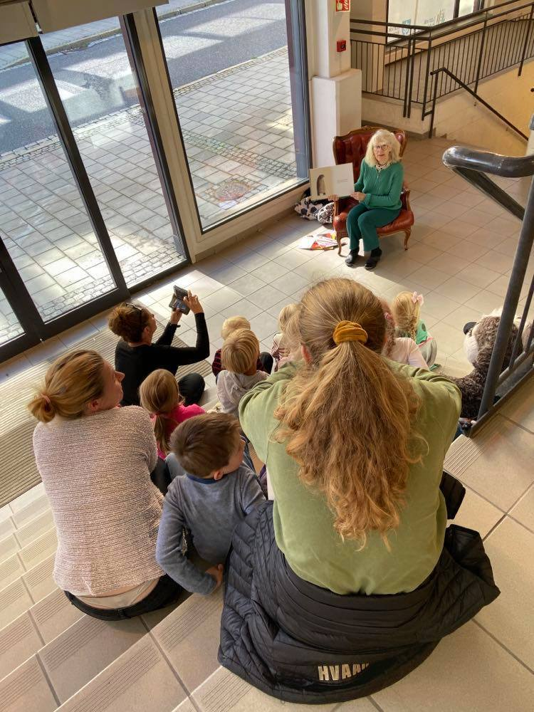 Barn og voksne sitter i trappen og blir lest for av bibliotekar Helga Frengstad. Foto
