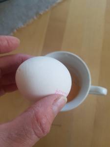 Egg med et lite hull i holdes over en kopp. Foto