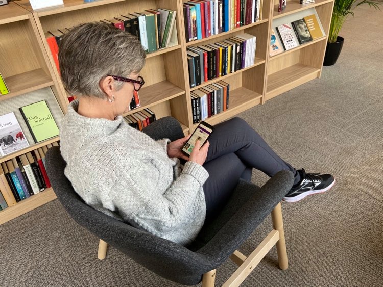 En kvinne sitter med sin mobil og leser bøker. Foto