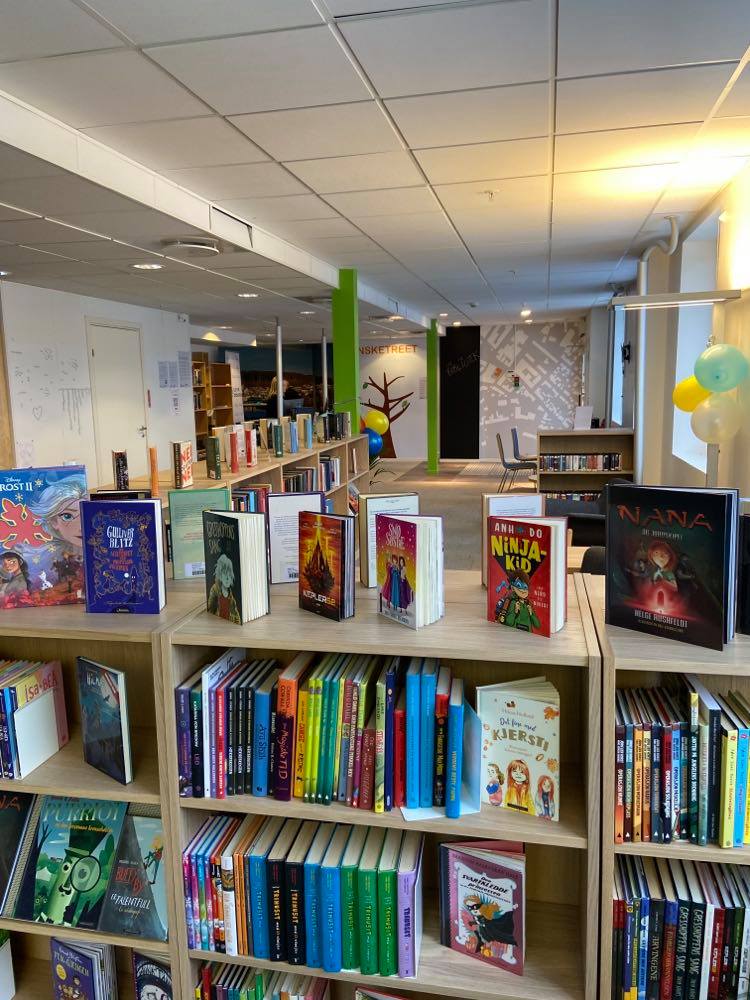Bibliotekinteriør med lave bokhyller og utstilte bøker på toppen av hyllene. Foto