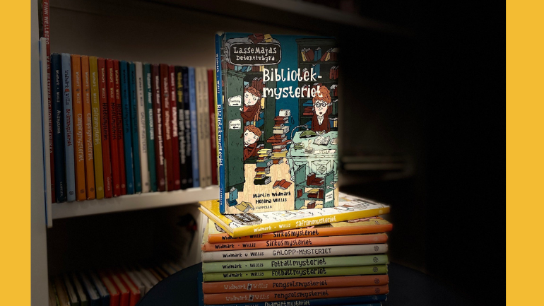 Foto av bøkene i serien Lassa Majas detektivbyrå i en bunke foran en bokhylle med bøker.