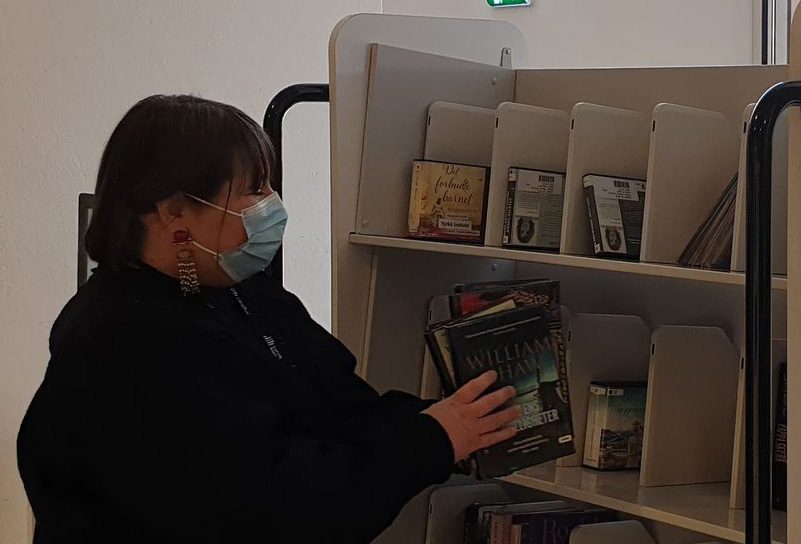 En person med munnbind setter bøker inn i en innleveringshylle. Foto