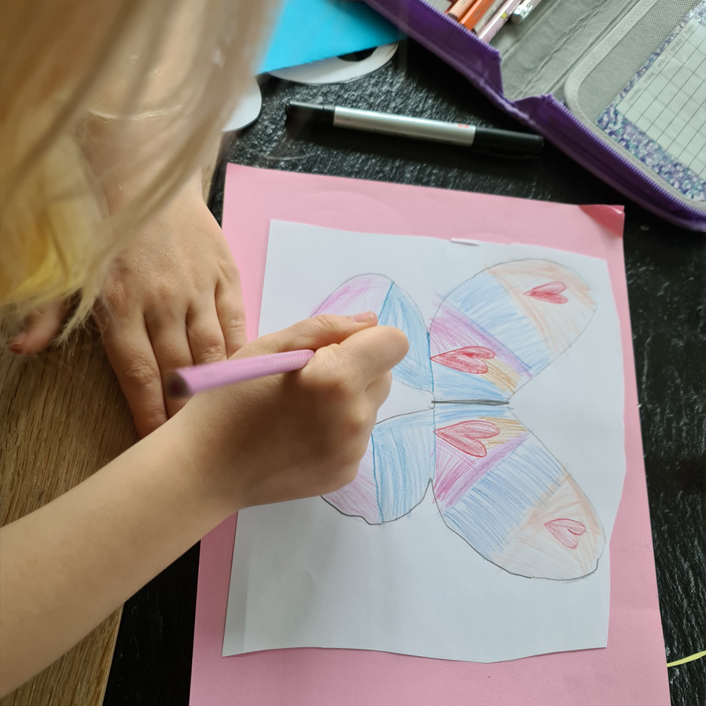 ei jente tegner en sommerfugl på hvitt ark. Foto