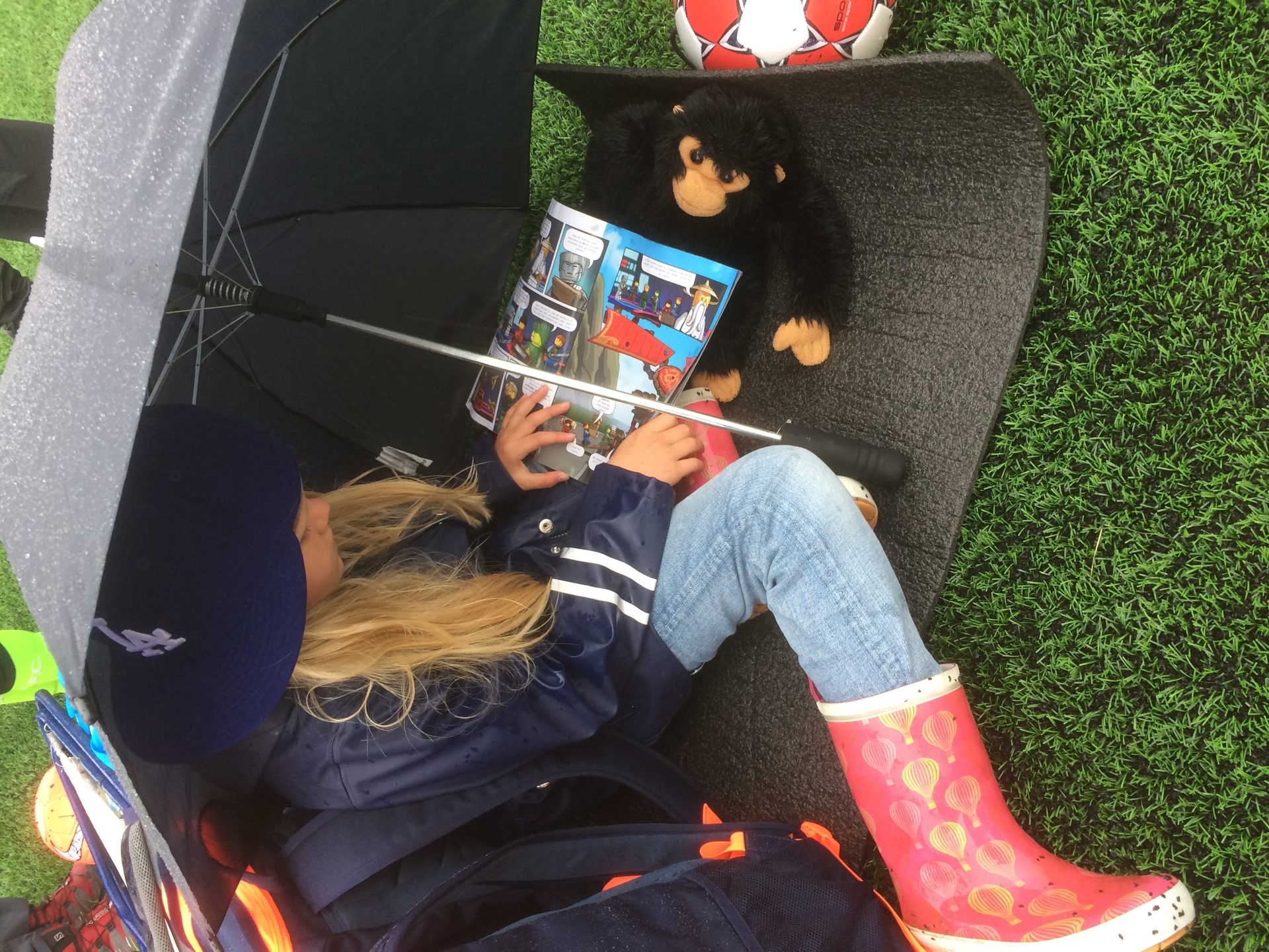 Jente sitter under paraply og leser. Foto