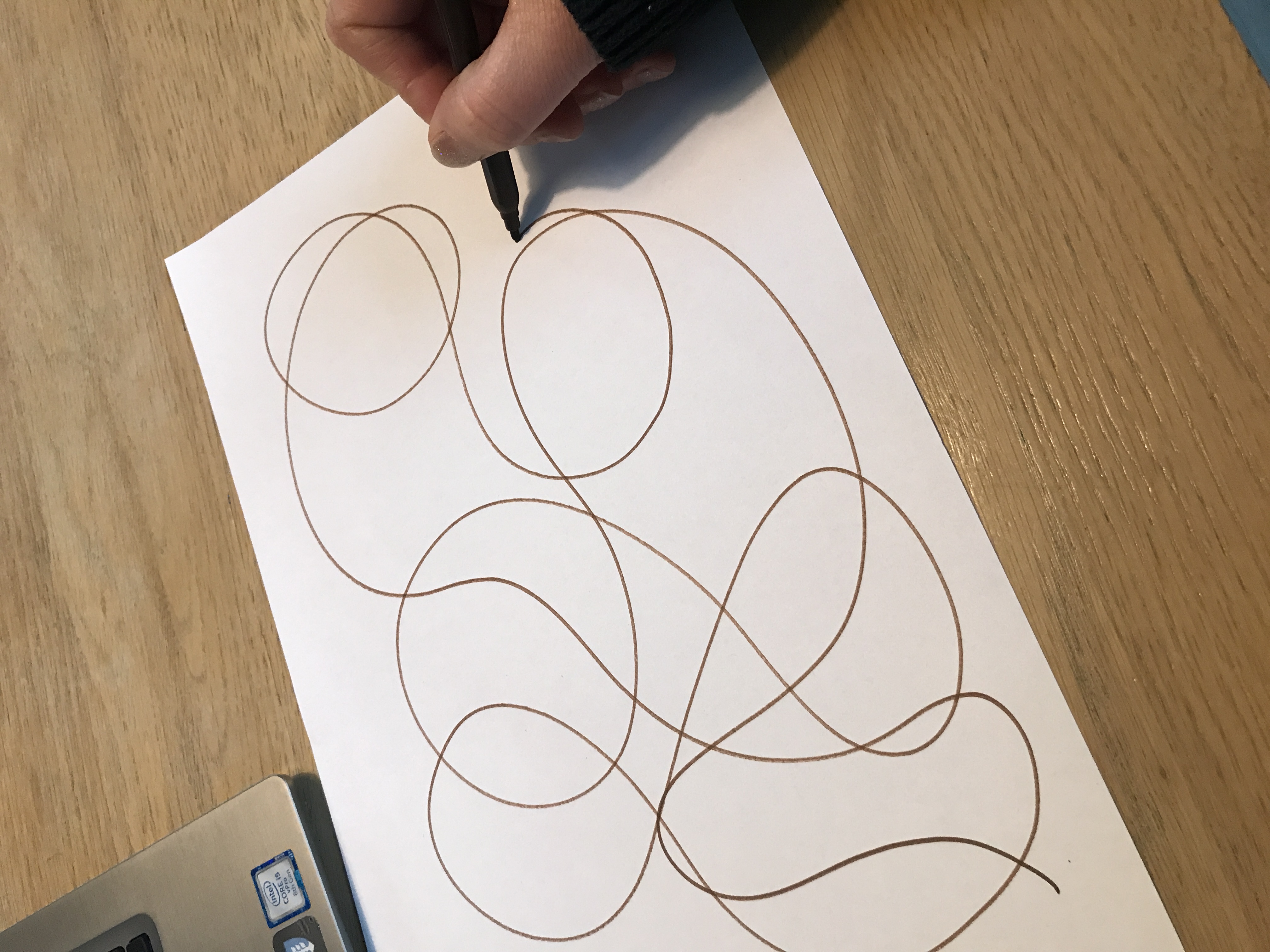 En hånd tegner kruseduller med blyant på papir. Foto