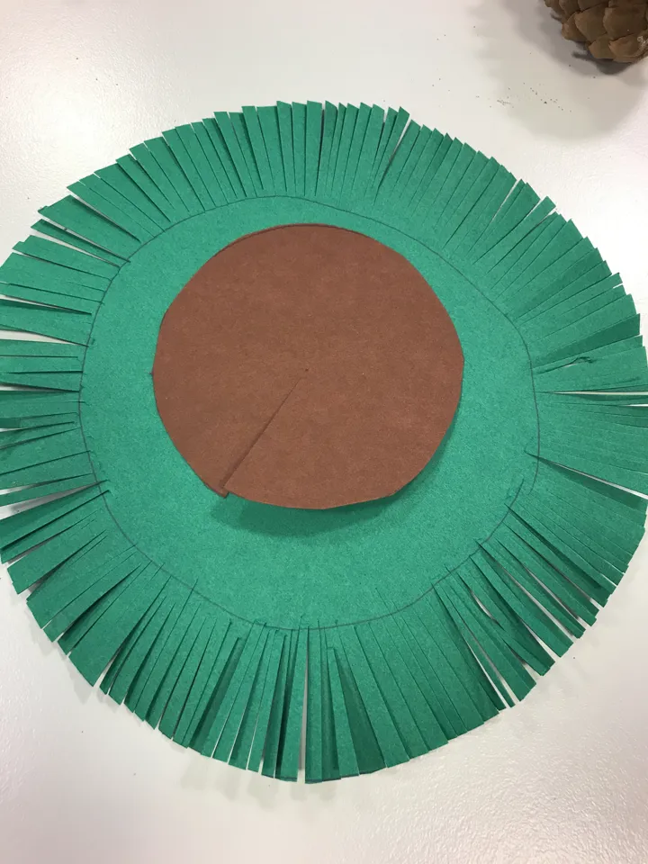 Bildet viser en runding av grønt papir, den er klippet opp i kanten, og en runding av brunt papir der det er klippet inn mot midten. Foto