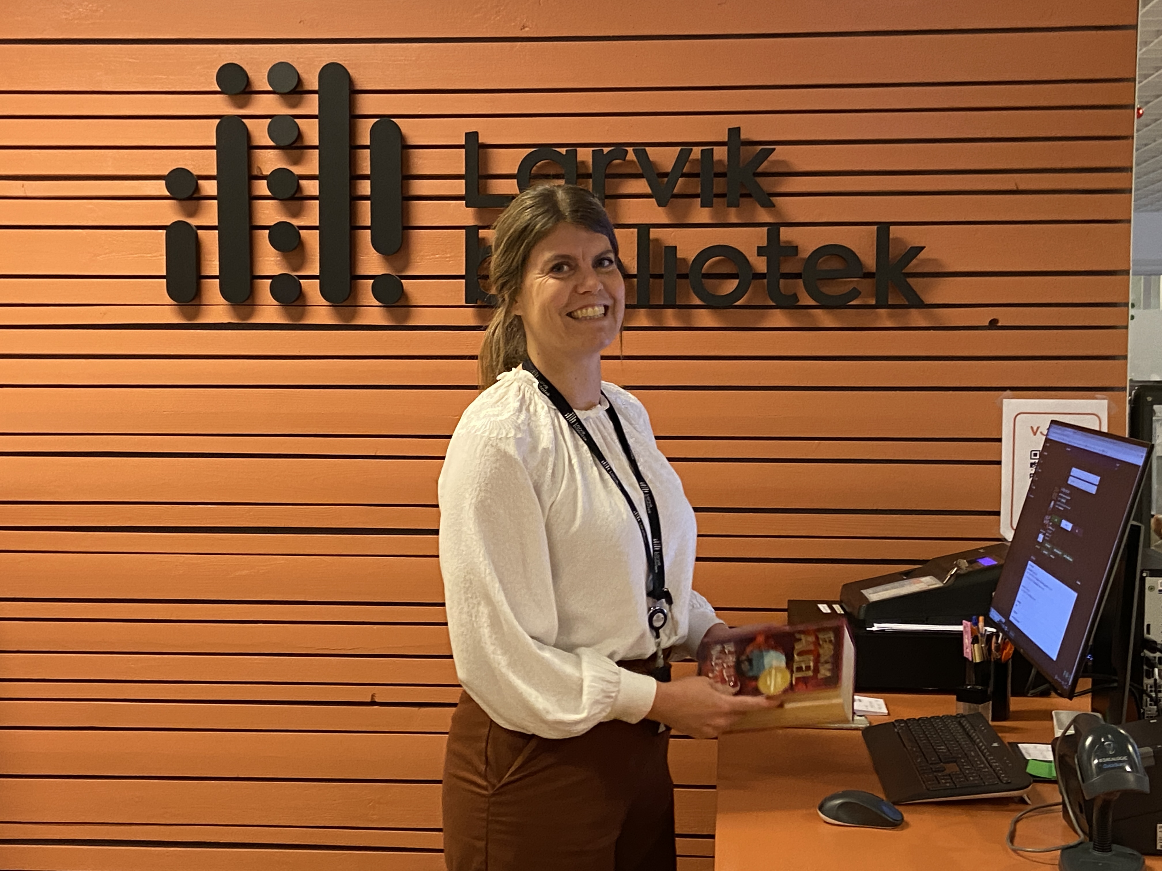 En kvinnelig bibliotekar ønsker velkommen i skranken på Larvik bibliotek. Foto