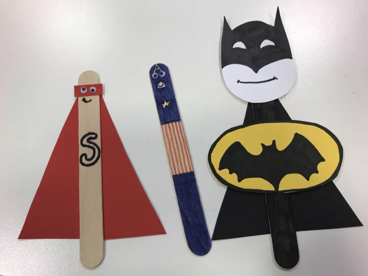 Tre superheltfigurer laget av ispinne og farget papir, og med tegninger med tusj. Foto