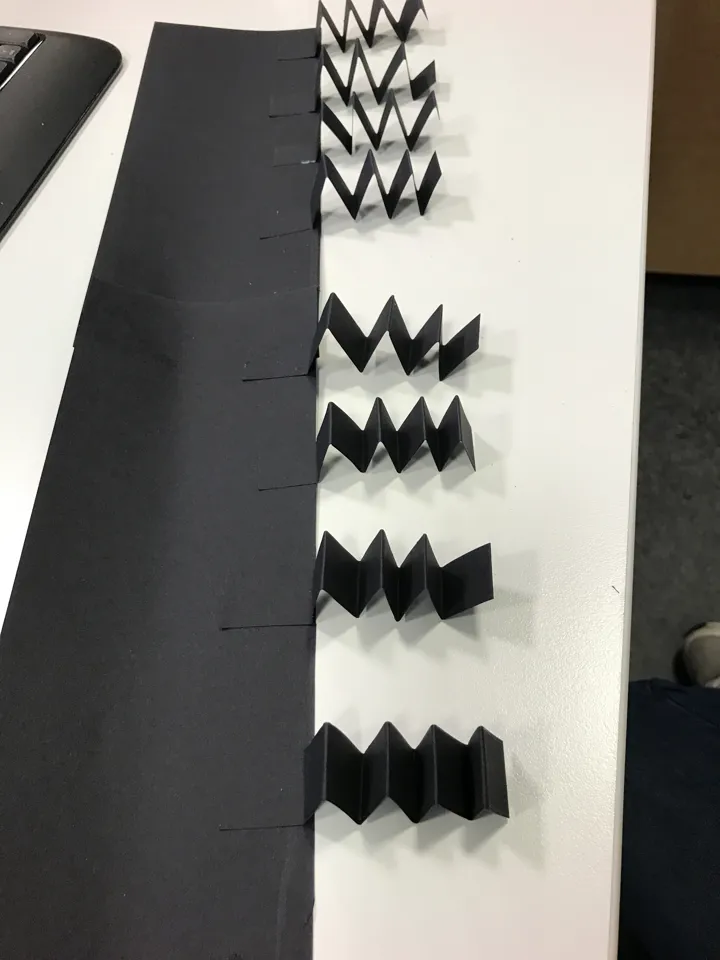 Bildet viser papirremser som er brettet som trekkspill og limt på et svart ark. Foto