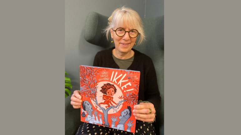 Foto av bibliotekar Helga. Hun sitter i en stol mens hun viser frem boka Ikke av Gro Dahle og Svein Nyhus.