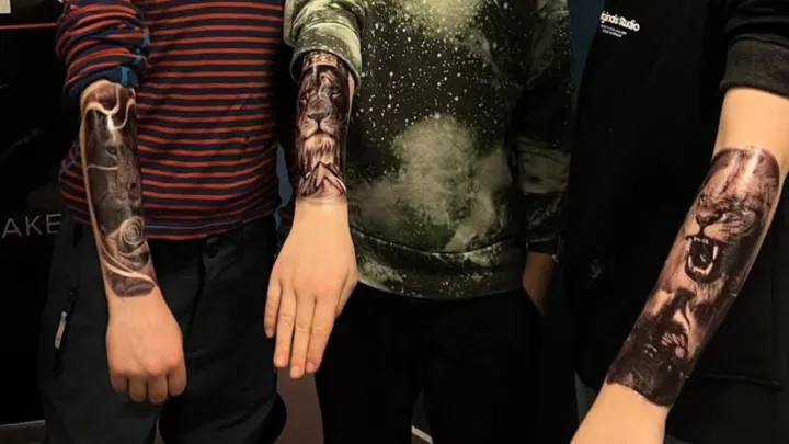 tre barn viser frem hver sin tatovering på armen. Vi ser kun armene, ikke barnas ansikter. tatoveringene er av løver. Foto