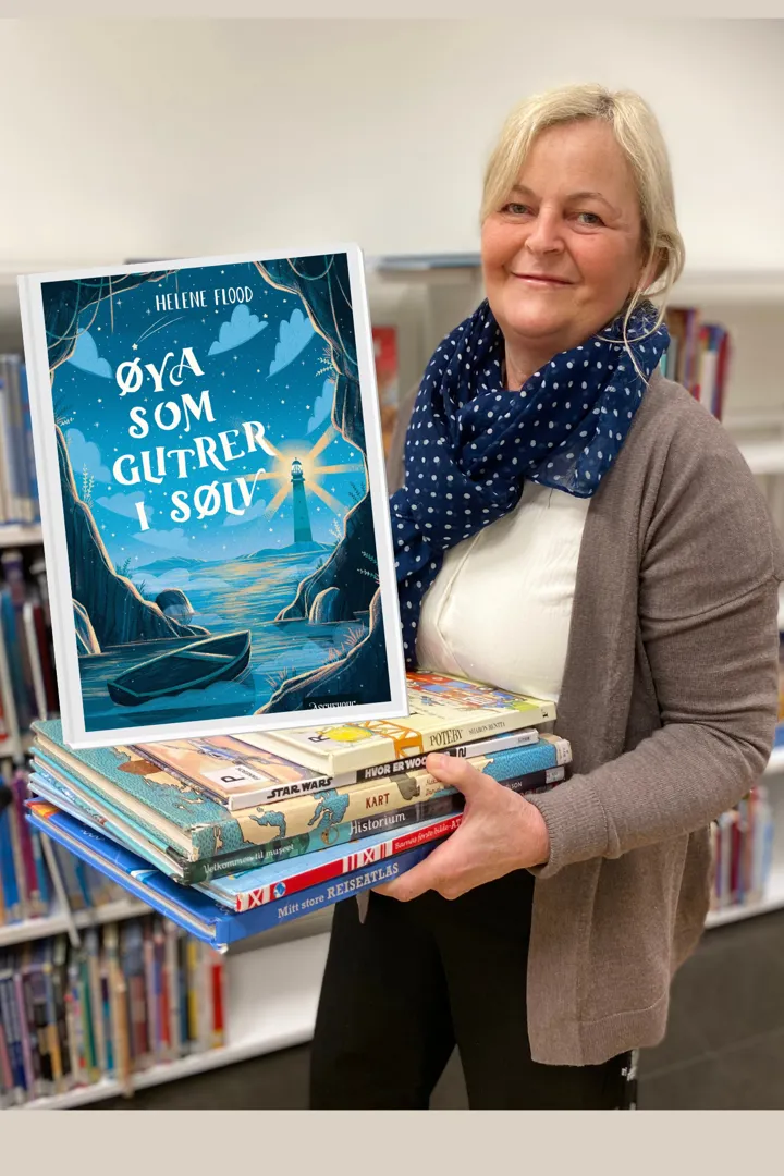 En av bibliotekets ansatte står foran en hylle full av bøker, hun smiler og hendene holder hun en bunke bøker. På bildet vises bokomslaget til Øya som glitrer i sølv.