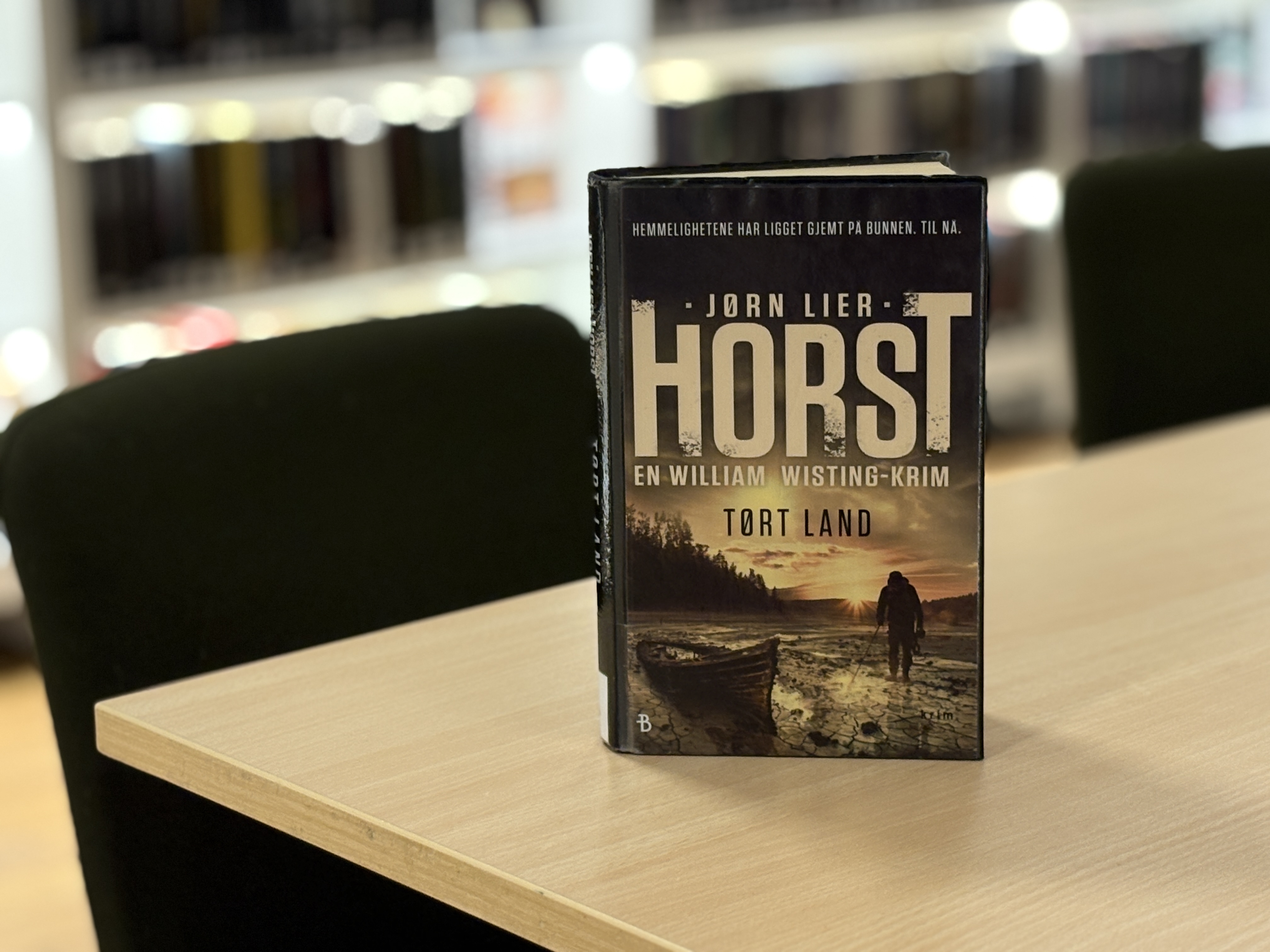 Boka "Tørt land" står oppstilt på et bord, man skimter bokhyller i bakgrunnen. Foto