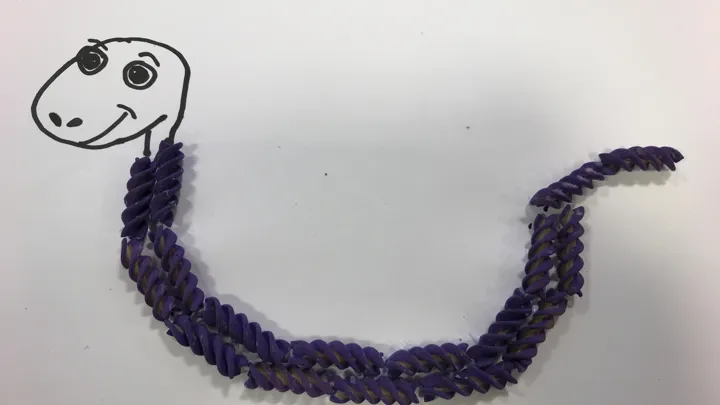 En liten og blid slange med pastakropp. Tegning med pålimt pasta. Foto