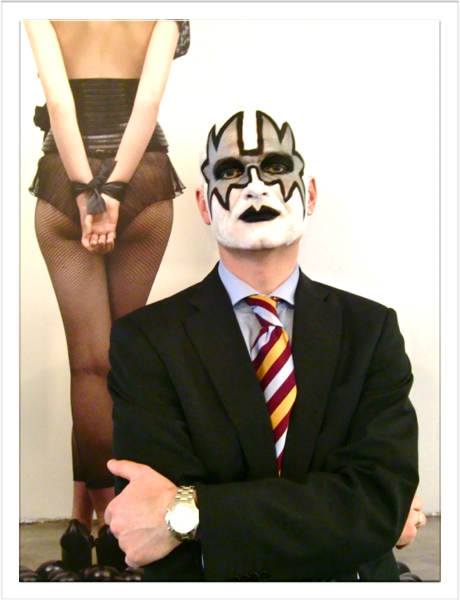 Fargefoto. Mann malt i ansiktet som en KISS-figur. Står foran en plakat med en dame sett bakfra.