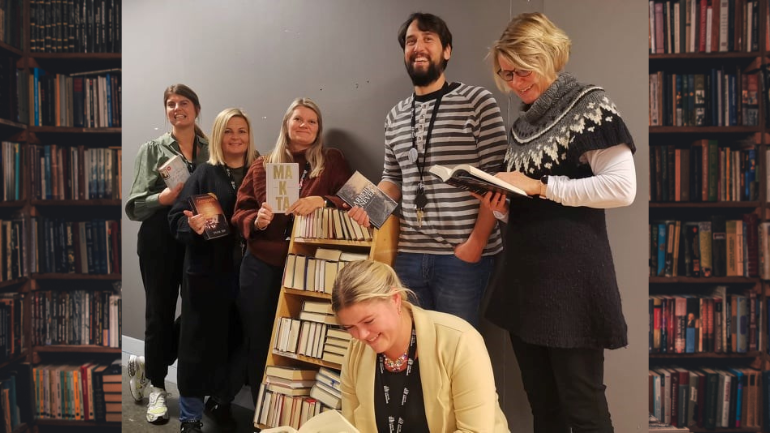 Seks av bibliotekets personale står rundt en tralle med bøker, de smiler og viser frem noen av bøkene