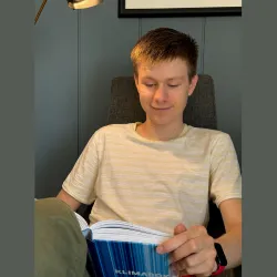 En ung mann sitter i en lenestol og leser i en bok som ligger i fanget hans. Foto: Paul Gjone