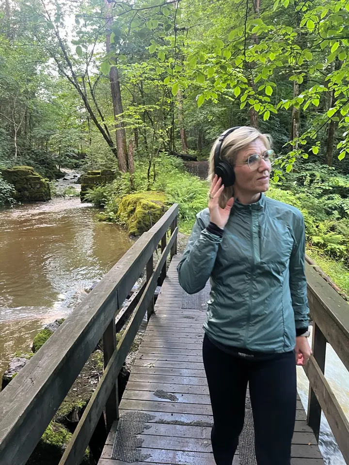 Kvinne med hodetelefoner på bru over vann i skogen. Foto: Privat