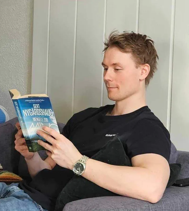 Ung gutt sitter i sofa og leser i en bok. Foto
