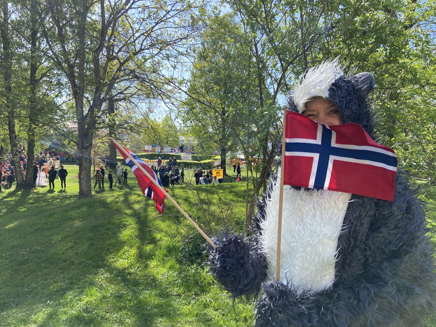 Maskoten GrevLing står med to norske flagg og koser seg utendørs. Foto