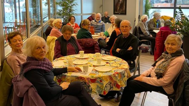 Seniorer sitter ved runde bord og koser seg med kaffe og kaker