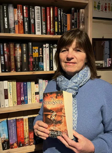 Portrett av Hanne Bergstrøm Odberg som står foran en bokhylle med en bok i hendene. Foto